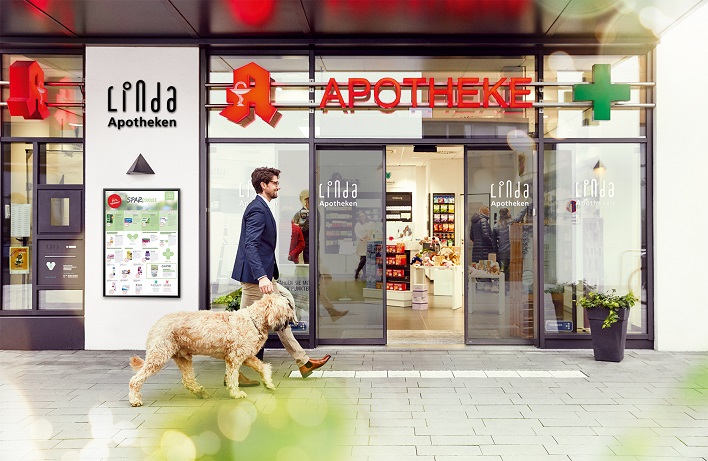 Eingang einer Linda Apotheke mit Passant und einem Hund.