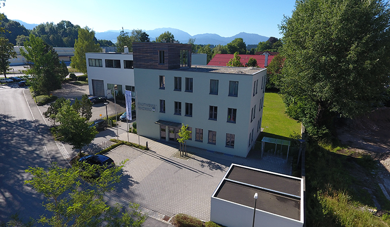 Luftaufnahme des modernen Gebäudes der Hautarztpraxis Oberland mit umliegender Natur und Bergen im Hintergrund