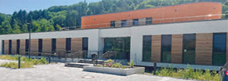 Moderne Gebäude mit Holz- und Glaselementen, umgeben von Grünflächen.