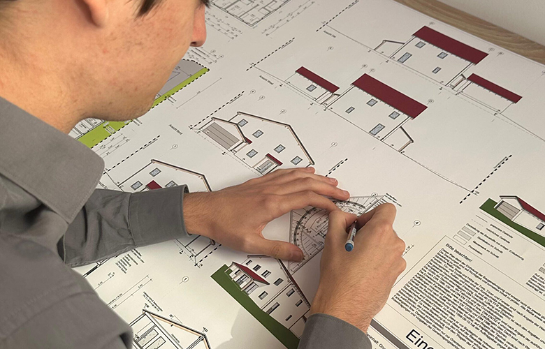 Nahaufnahme eines Mannes, der mit einem Geodreieck und einem Stift an einem großformatigen Bauplan oder architektonischen Entwurf arbeitet