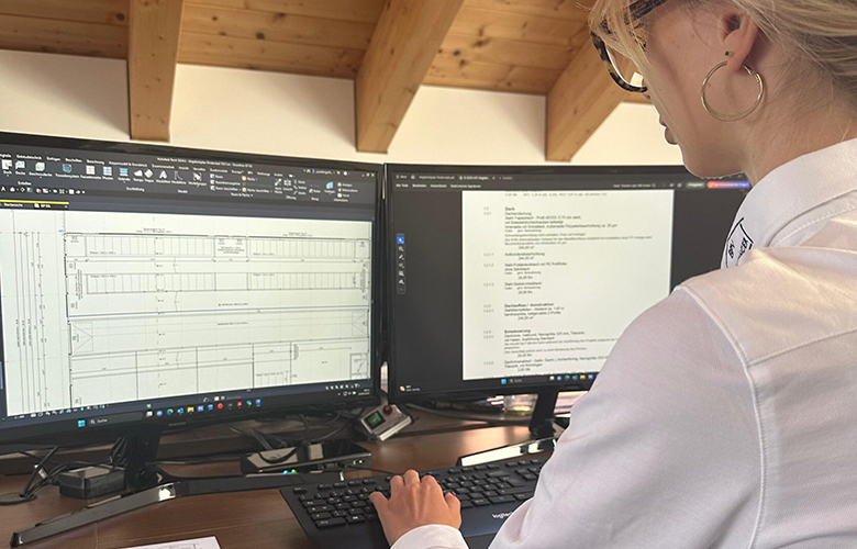 Frau in einem weißen Hemd sitzt an einem Schreibtisch und arbeitet an zwei Computermonitoren