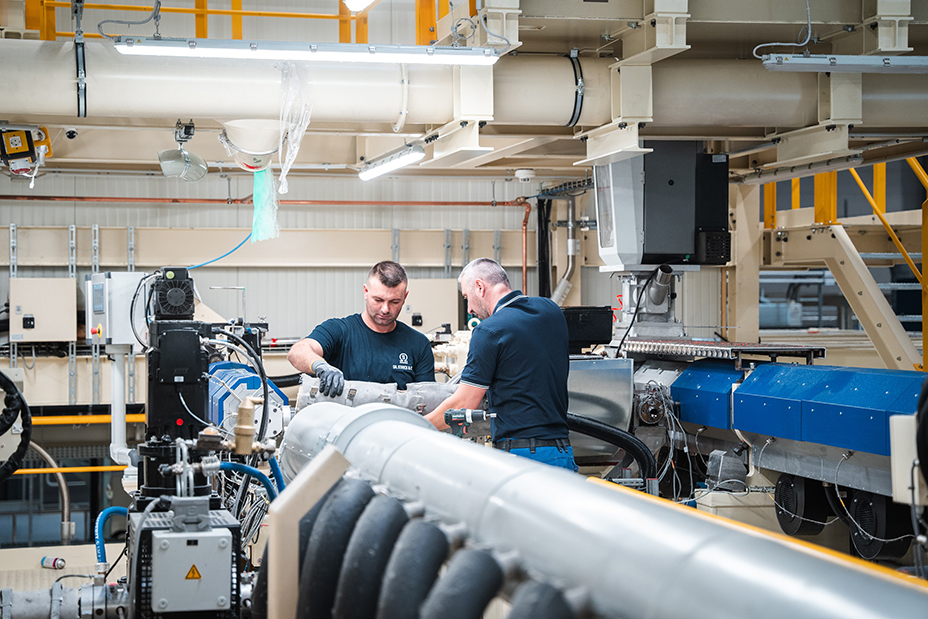 Zwei Fachkräfte arbeiten gemeinsam an komplexer Maschine in moderner Produktionshalle