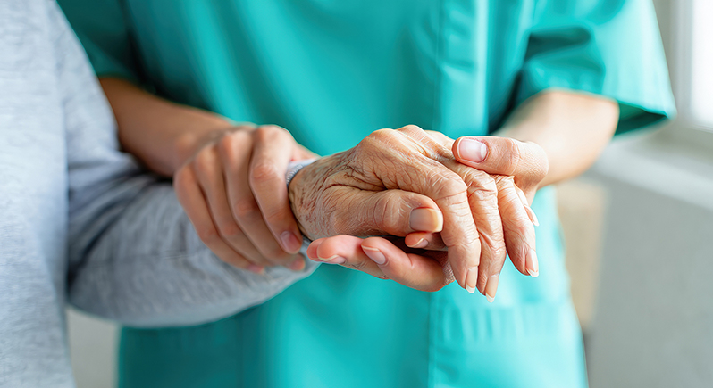 Nahaufnahme einer Pflegekraft, die schützend die Hand eines älteren Menschen hält