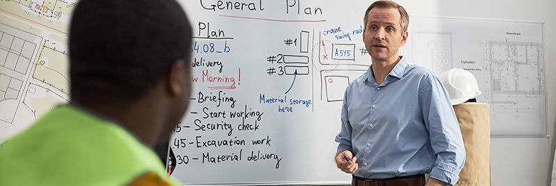 Bauleiter erklärt Tagesplan am Whiteboard