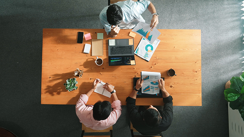 drei Personen arbeiten um den Tisch herum