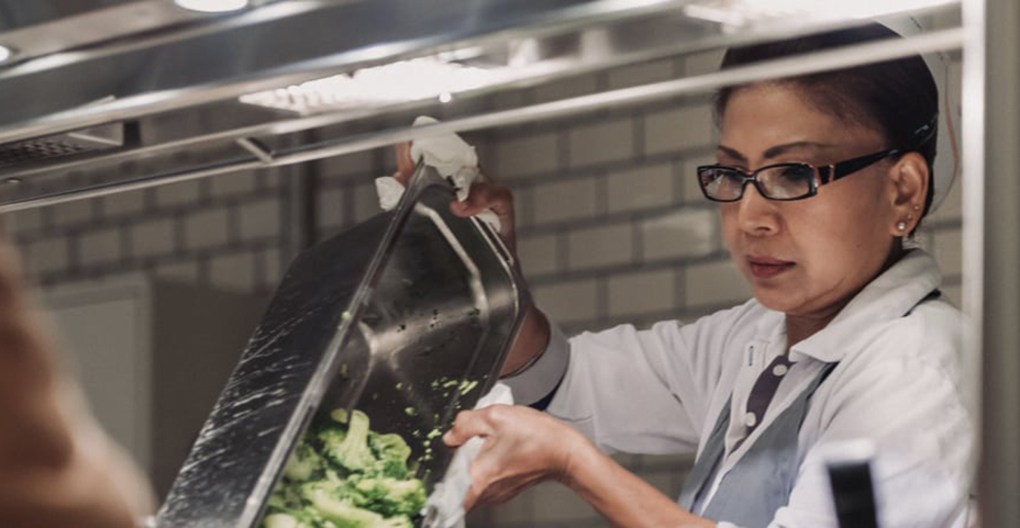 Köchin füllt frischen Brokkoli aus einem Metallbehälter um