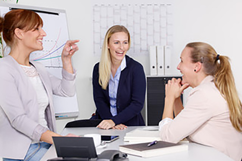 Drei Frauen lachen bei Teambesprechung vor Flipchart