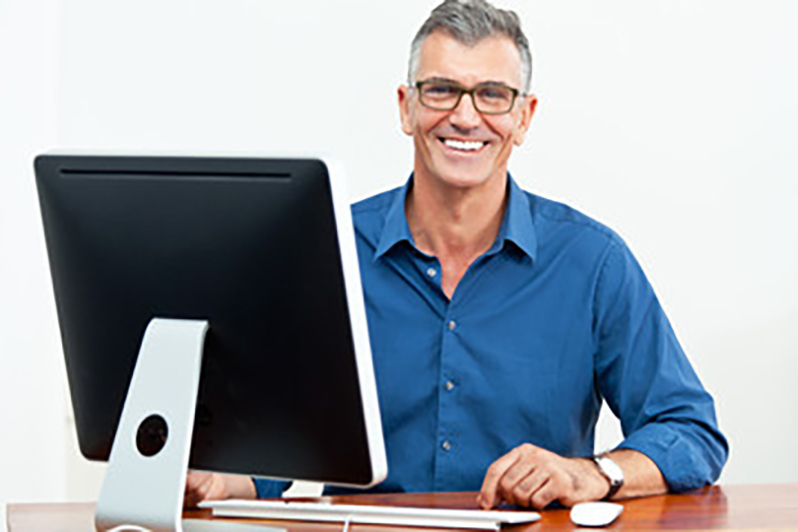 Lächelnder Mann mit Brille sitzt am Computer