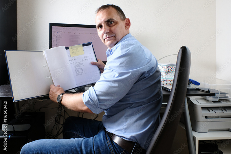 Mann am Schreibtisch hält Aktenmappe vor Computer