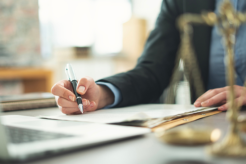 Hand unterzeichnet Vertrag neben Justitia-Figur