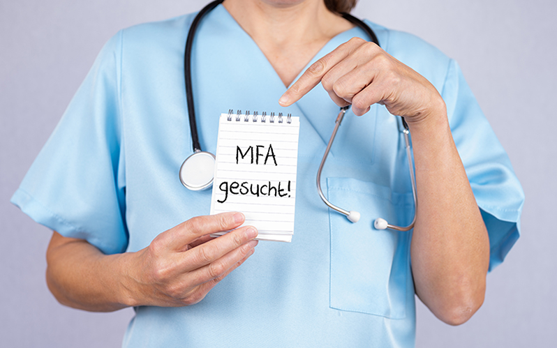 Eine Krankenschwester hält einen Zettel „MFA gesucht“.