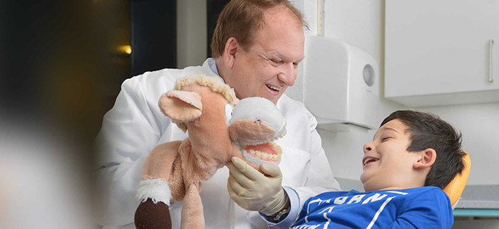 Zahnarzt erklärt einem Kind spielerisch die Zahnpflege mit einer Handpuppe