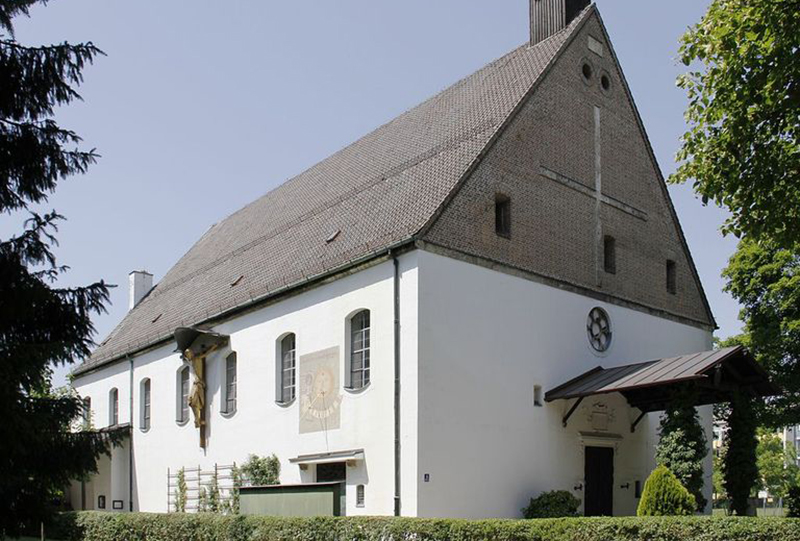 Weiße Kapelle mit hohem Steindach, Sonnenuhr an der Fassade und Kruzifix