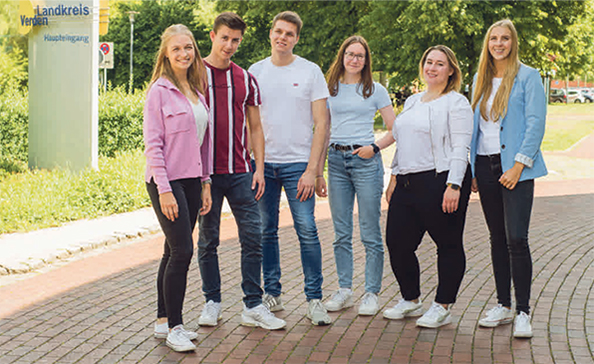Sechs lächelnde junge Erwachsene stehen nebeneinander