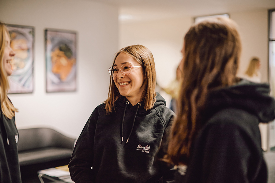 Drei junge Frauen im Sprehe-Hoodie unterhalten sich