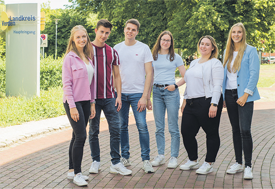 Sechs lächelnde junge Erwachsene stehen nebeneinander