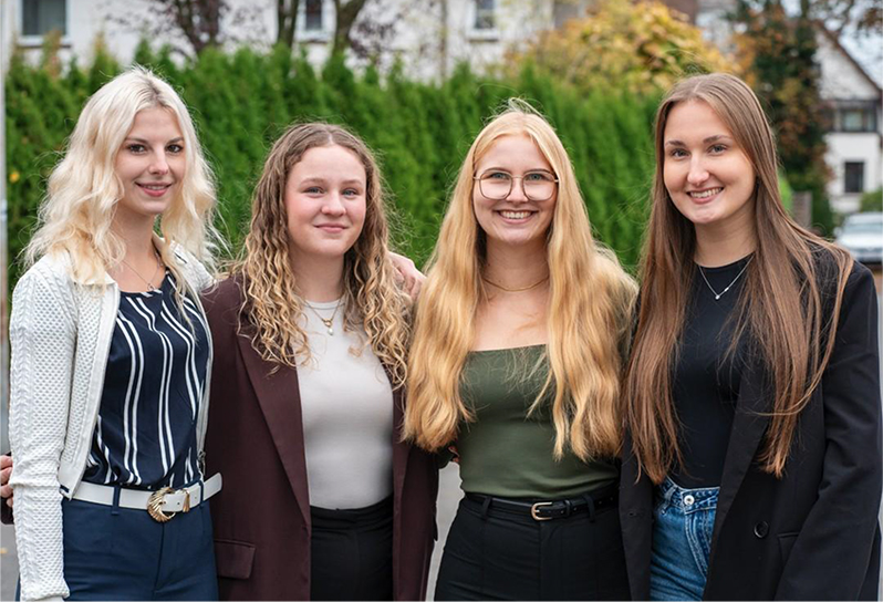 Vier junge Frauen stehen lächelnd nebeneinander