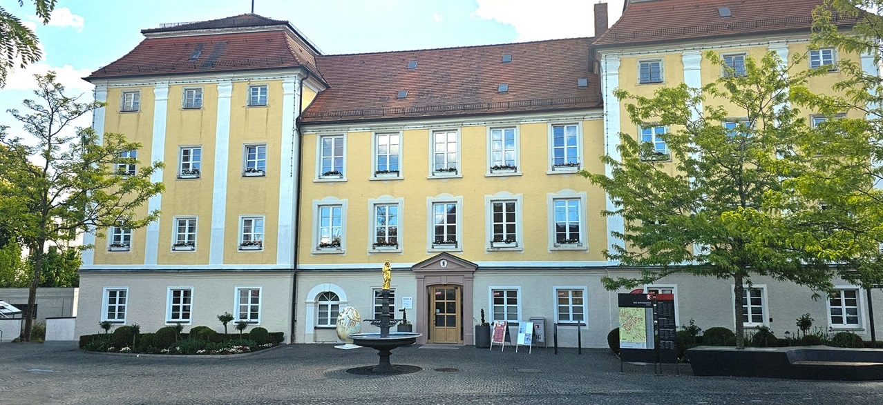 Gelbes Gebäude mit Brunnen davor.