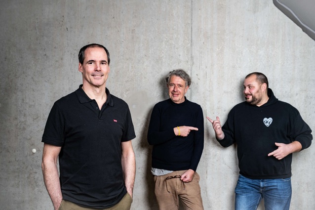 Drei Männer vor Betonwand.