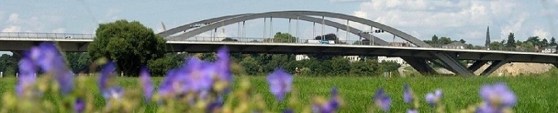 Blick auf eine Rundbogenbrücke mit Blumen und einer Wiese im Vordergrund