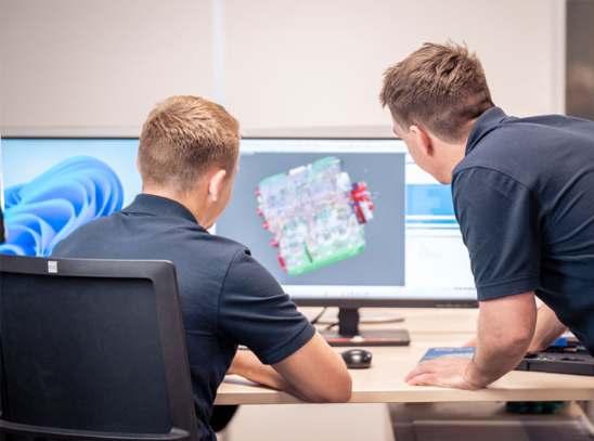 Zwei Männer betrachten einen Monitor mit einer 3D-Skizze darauf.