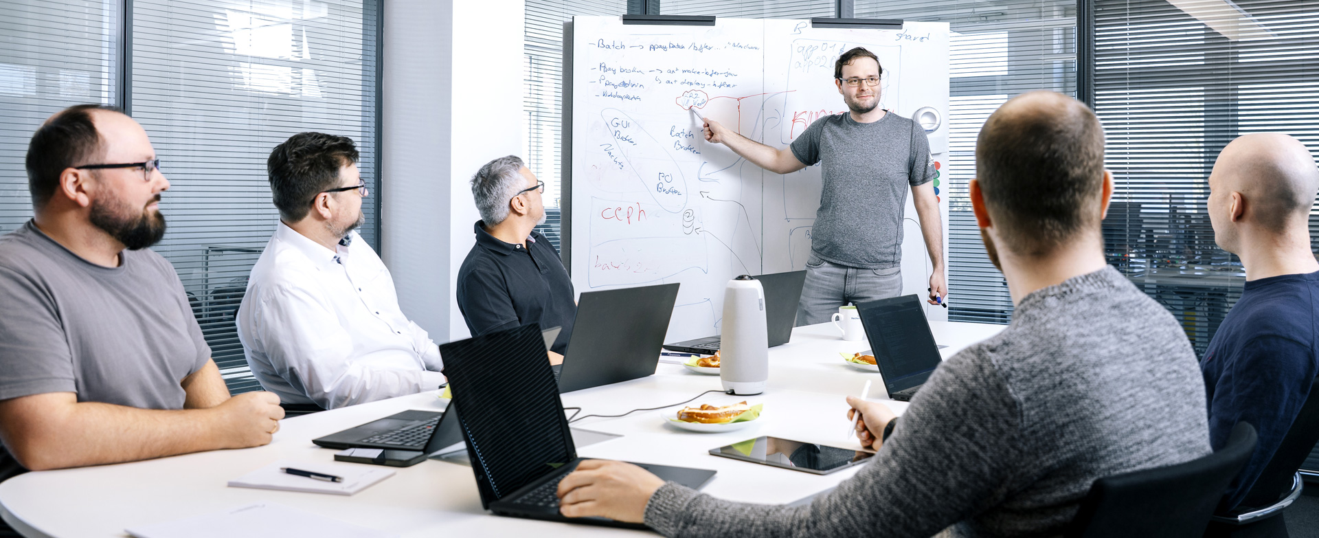Ein Team aus drei Kollegen arbeitet gemeinsam an einem Laptop und lacht in einem hellen Büro.