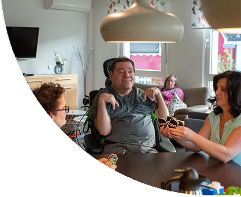 Personen sitzen an einem Tisch in einem Wohnverbund und spielen UNO