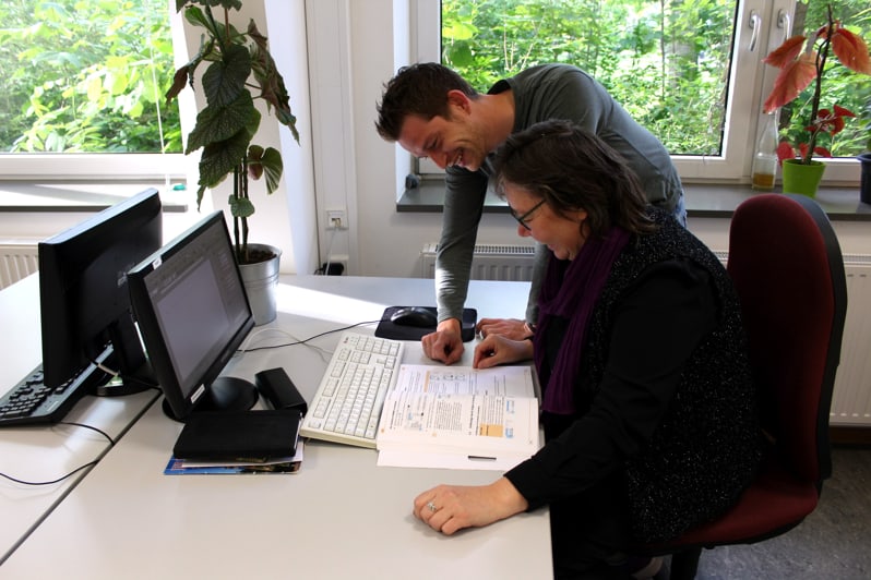 Ein Mann und eine Frau arbeiten lächelnd gemeinsam an einem Schreibtisch