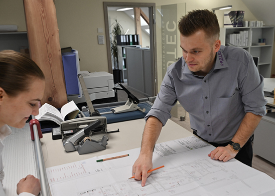 Zwei Personen besprechen technische Pläne in einem Büro