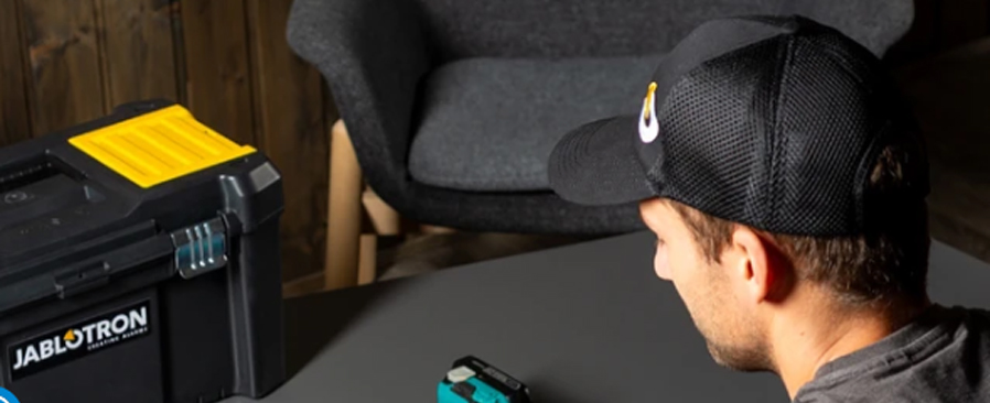 Jablotron-Techniker richtet Überwachungskameras mit einem Smartphone ein, neben einem Werkzeugkoffer und einem Akkubohrer auf einem grauen Tisch