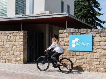 Eine Frau fährt mit dem Fahrrad am eology-Firmenschild vorbei