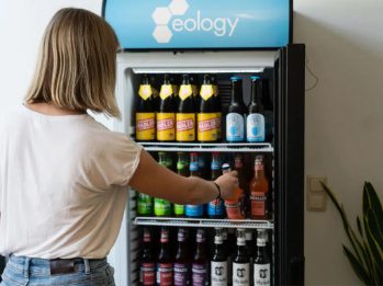 Eine Frau nimmt ein Getränk aus einem eology-gebrandeten Kühlschrank