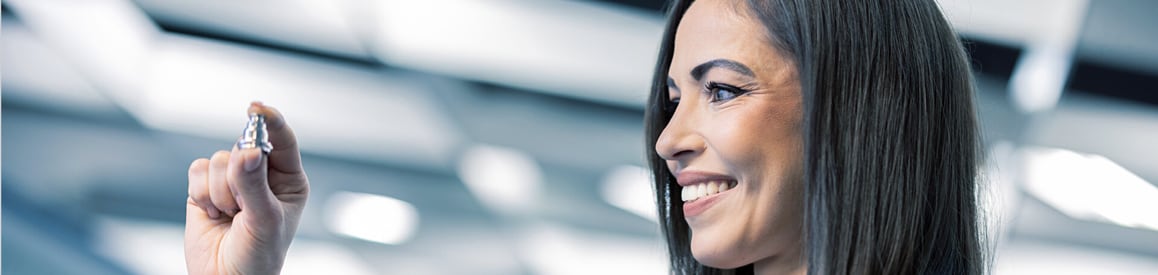 Lächelnde Frau hält präzises Metall-Kleinteil prüfend hoch