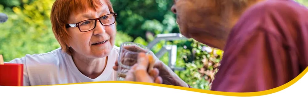 Brillenträgerin reicht einer Seniorin ein Glas Wasser