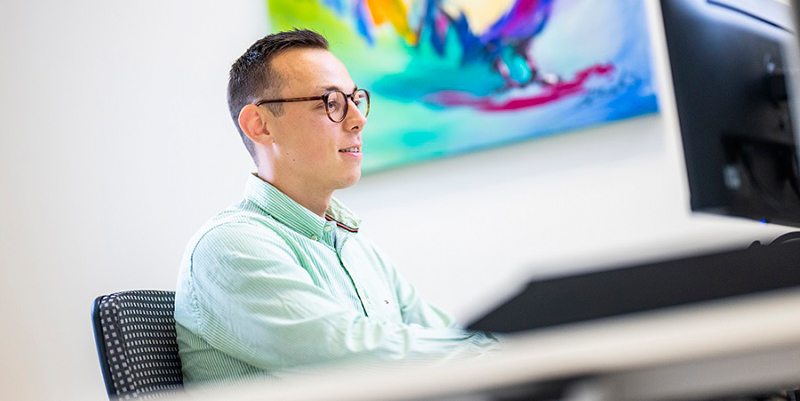 Junger Mann mit Brille im grün gestreiften Hemd arbeitet konzentriert am PC-Monitor im Büro