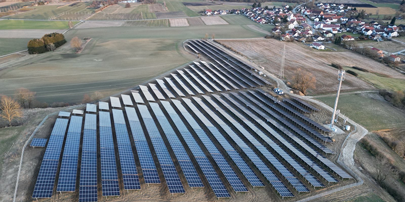 Luftbild einer Solaranlage am Ortsrand neben Feldern und einem Funkmast