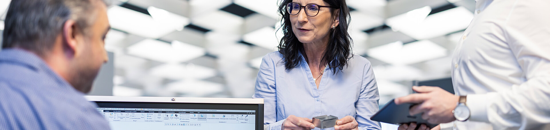 Mitarbeiterin mit Bauteil im Gespräch mit Kollegen