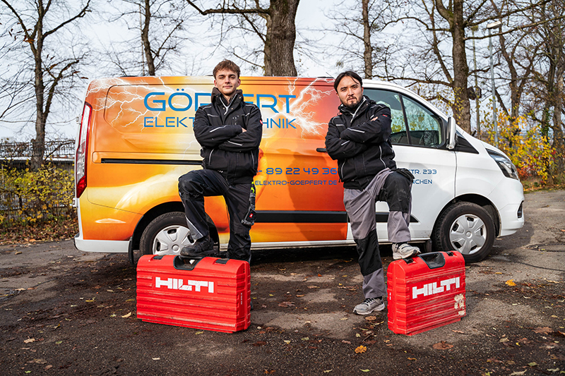 Zwei Elektriker posieren vor einem Firmenwagen