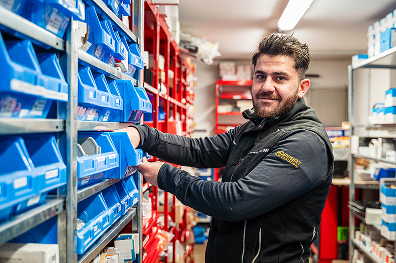 Mitarbeiter der Göpfert Elektrotechnik sortiert Kleinteile in blaue Lagerboxen eines Metallregals