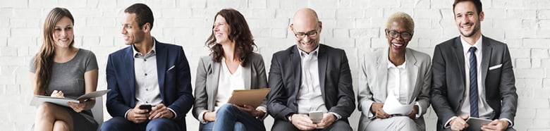 Sechs Personen sitzen lächelnd im Wartezimmer