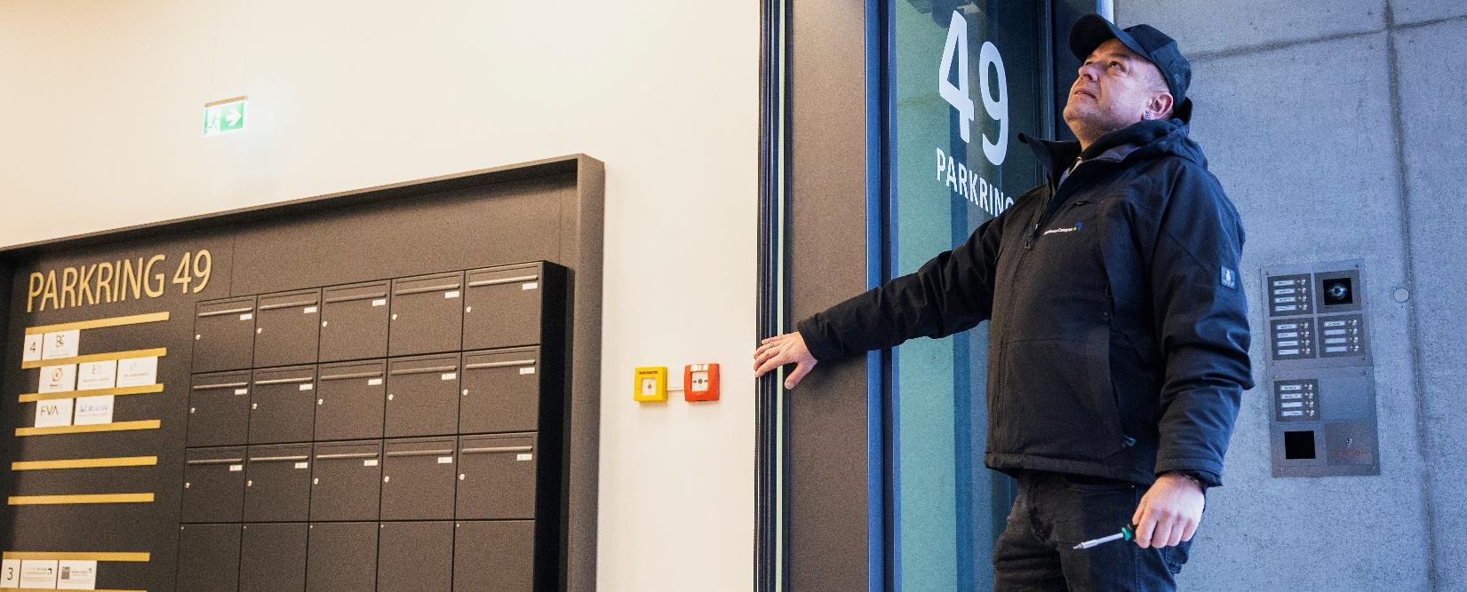 Handwerker mit Schraubendreher prüft Technik an einem modernen Gebäudeeingang