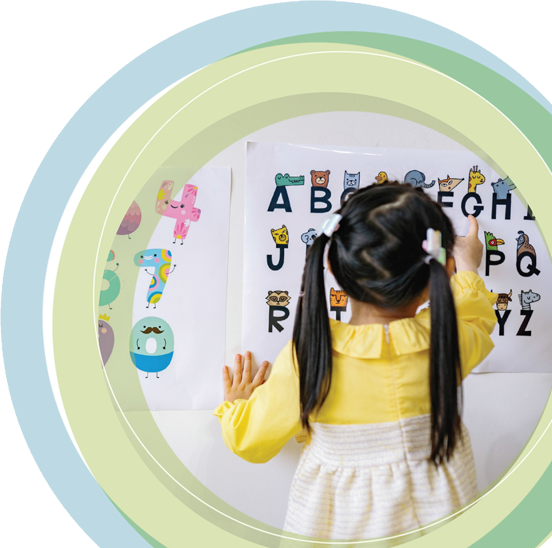 Mädchen mit Zöpfen zeigt auf ein Alphabet-Poster