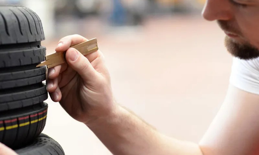Mechaniker prüft die Profiltiefe eines Autoreifens mit einem Messwerkzeug
