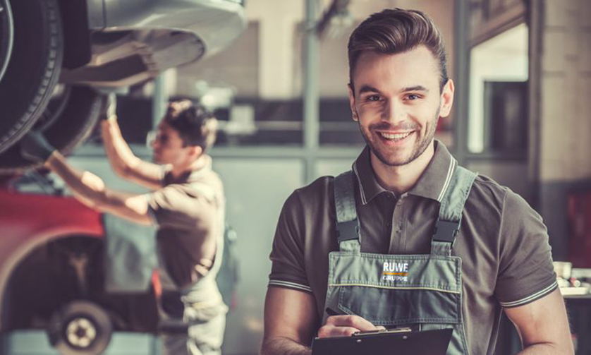 Lächelnder Mechaniker der Ruwe Gruppe mit Klemmbrett in einer Kfz-Werkstatt