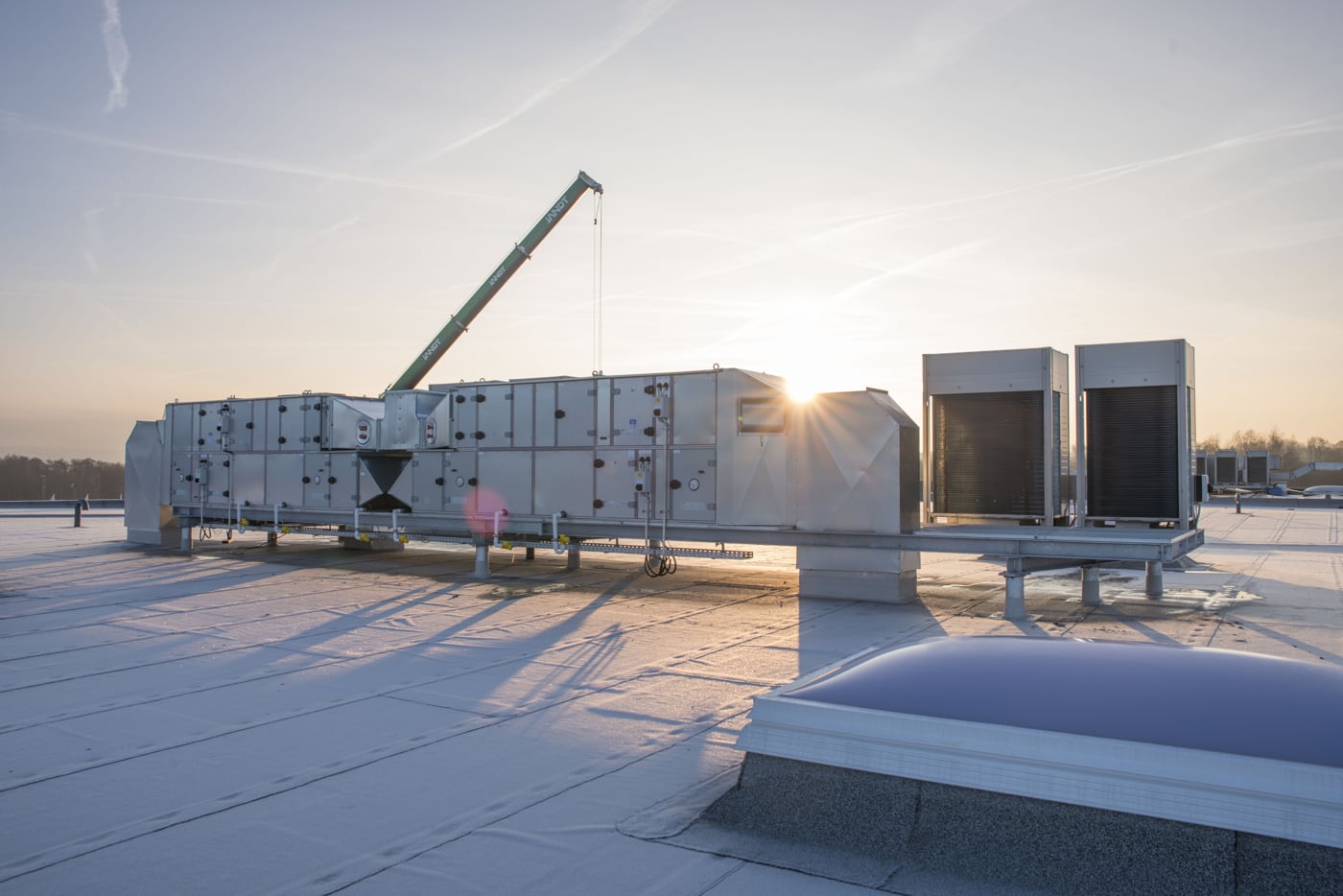 Industrie-Lüftungsanlage auf einem verschneiten Flachdach bei Sonnenaufgang