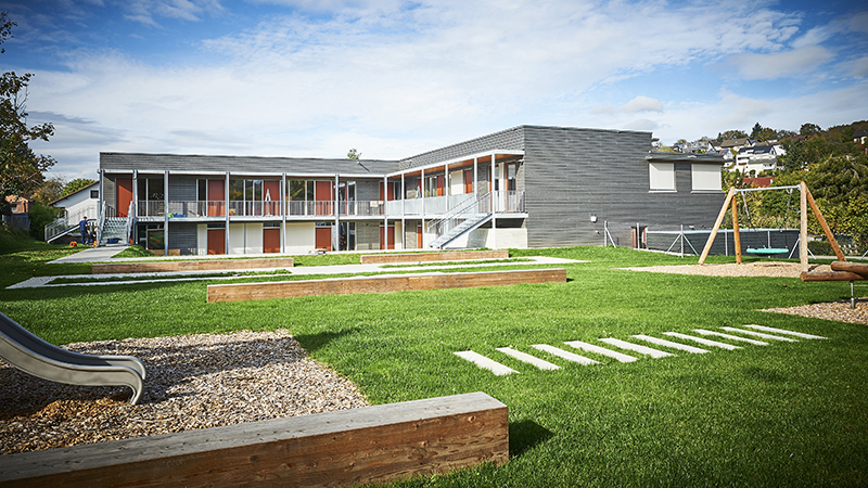 Moderner Kindergarten mit Holzfassade und großer Spielwiese