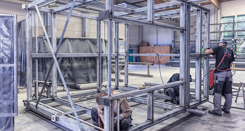 Bauarbeiter fertigen ein modulares Stahlrahmen-Skelett in einer Industriehalle