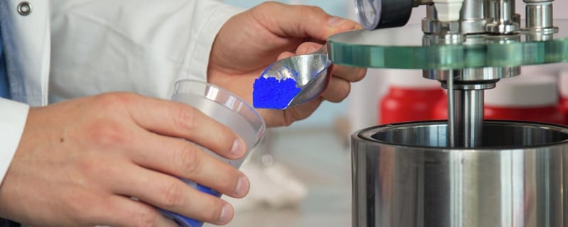 Laborant füllt blaues Pulver mit einer Metallschaufel in einen Becher um